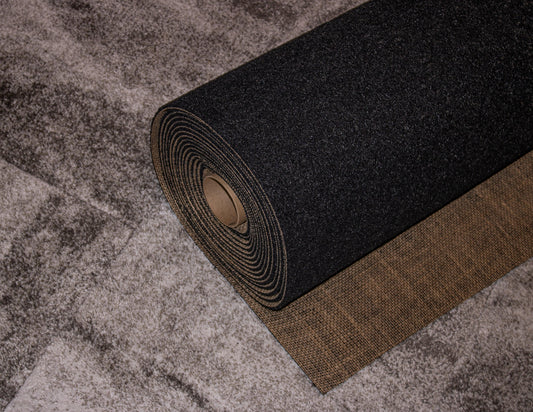 The Dura Undercushions' Duralux™ Comfort 7 mm, a luxurious black roll of carpet, seamlessly unrolls on a grey floor, showcasing high-end rug protection while enhancing style and functionality.