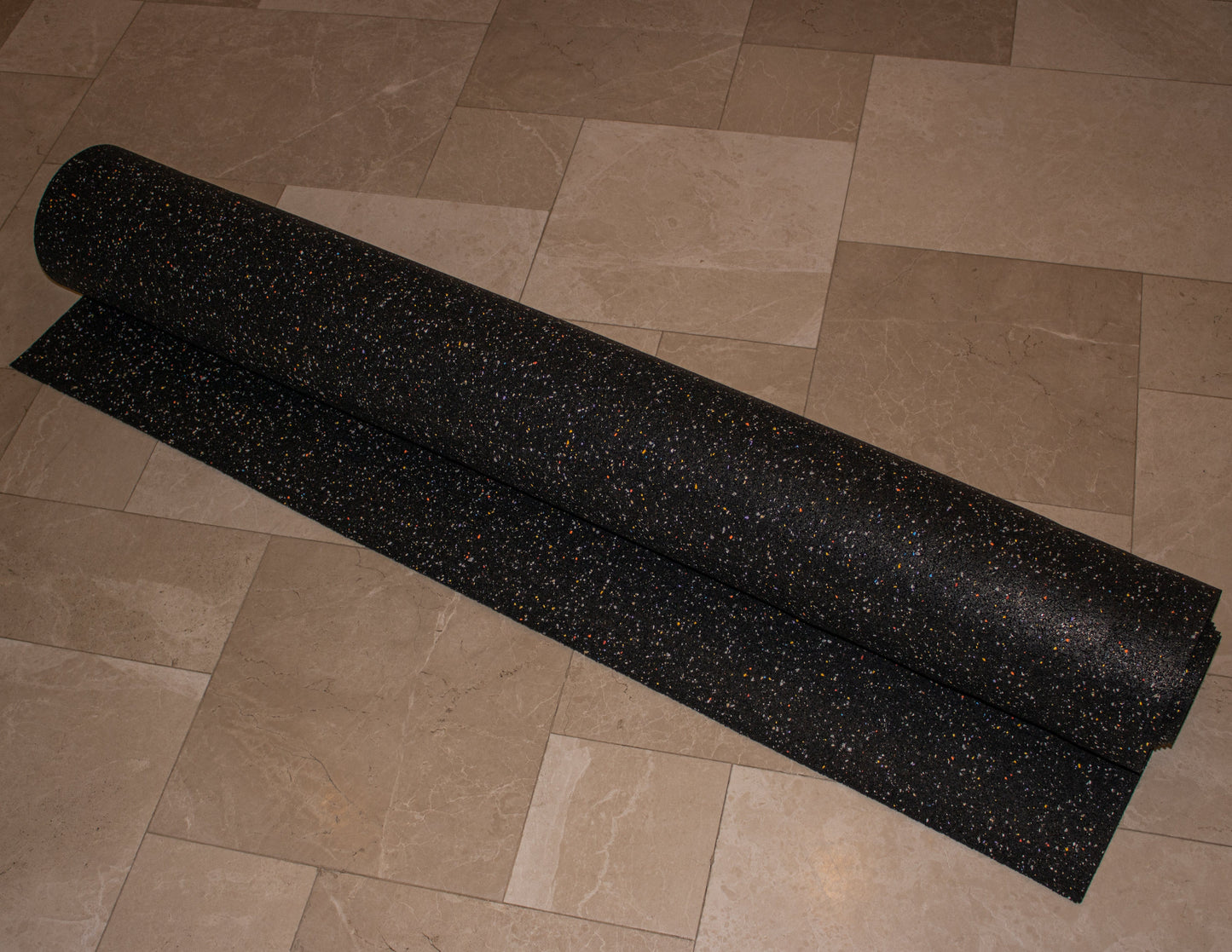 A rolled-up piece of Duraquiet™ 3 mm from Dura Undercushions, ideal as an acoustic underlayment, lies on a tiled floor.