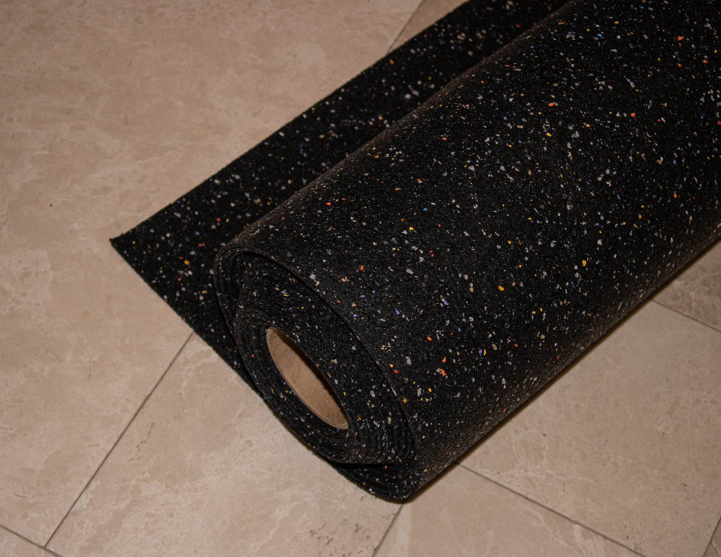 A roll of black rubber flooring with colored specks on a tiled surface, designed with Duraquiet™ 3 mm acoustic underlayment by Dura Undercushions for enhanced sound insulation.