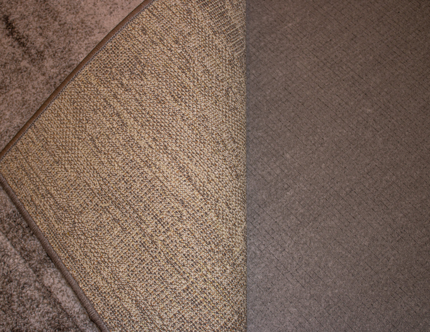 Close-up of the corner of a beige textured rug that has been partially folded over, revealing the Dura Undercushions Protector™ 5 mm carpet underlay and an adjacent section of the floor.